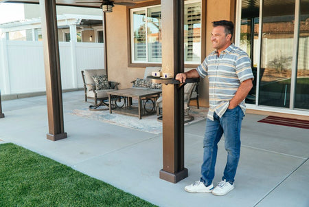 Smiling man leaning against an Alumatable mounted on his patio cover post with two drinks also resting on the table