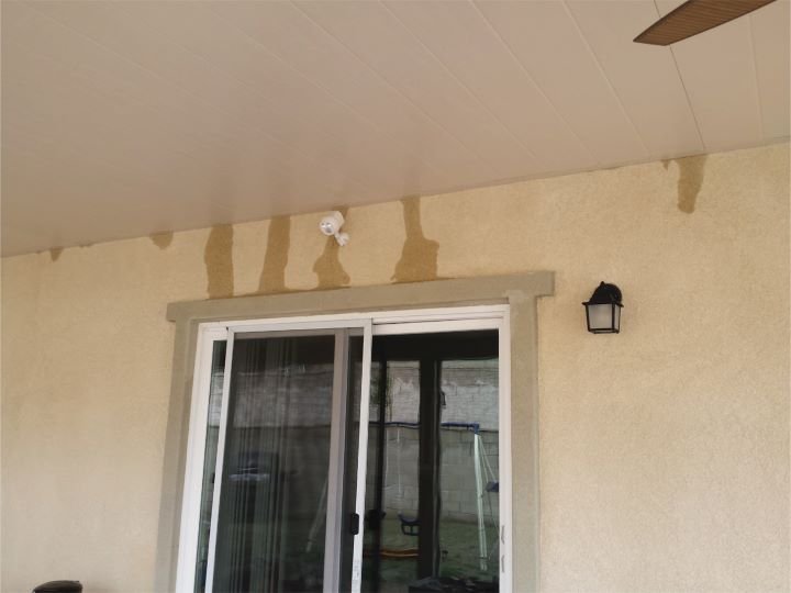 Stucco wall below an aluminum patio cover showing “leaks.”